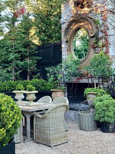 an outdoor dining table surrounded by potted plants and greenery with a fireplace in the background