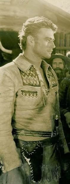 an old black and white photo of a man in native garb standing next to other men