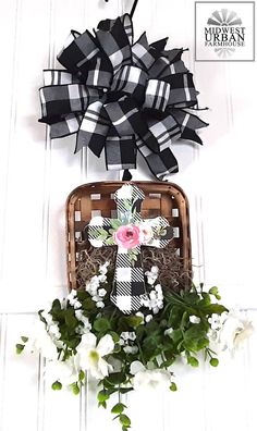 a cross is hanging on the wall next to some flowers and a basket with ribbon