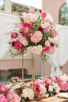 pink and white flowers are arranged in gold vases on a table at a wedding