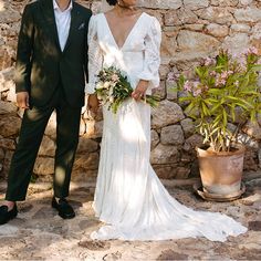 a man and woman standing next to each other in front of a stone wall holding hands