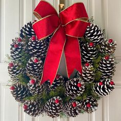 a christmas wreath with pine cones and red ribbon