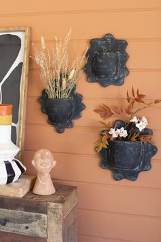 three pots with flowers are hanging on the wall next to a wooden box and vase