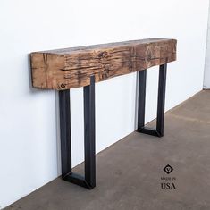 a wooden bench sitting on top of a cement floor next to a white wall with black metal legs