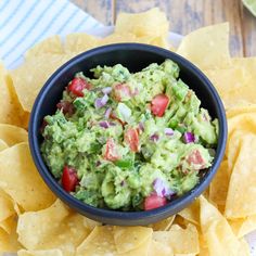 a black bowl filled with guacamole surrounded by tortilla chips