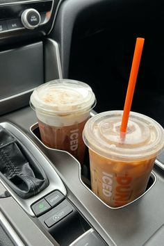 two iced coffees are sitting in the center console of a car