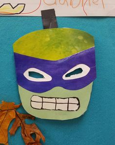 a paper mache with a green and purple mask on it's face next to leaves