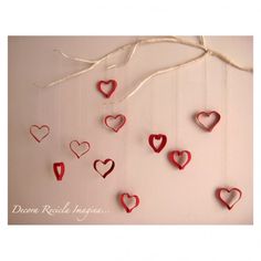 red hearts hanging from a tree branch on a wall with white string and twine