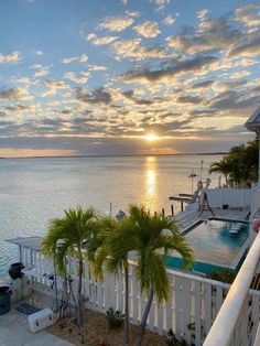 the sun is setting over an ocean with palm trees and a house in the foreground