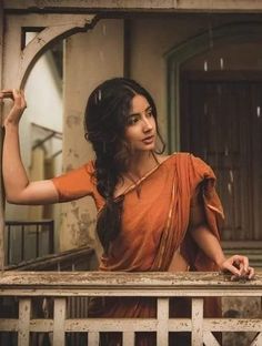 a woman in an orange sari is standing on a porch with her arms outstretched