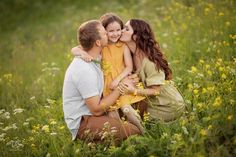 a family is sitting in the grass and hugging each other