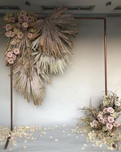 dried flowers are arranged in front of a white wall with two metal poles on it