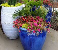 three large vases filled with different types of flowers and greenery on a patio