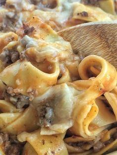 a casserole dish with meat, cheese and noodles in it on a wooden spoon