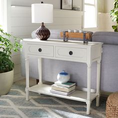 a white table with two drawers and a lamp on it in front of a couch