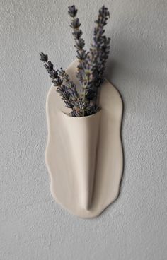 a vase with lavender flowers in it hanging on the wall next to a plaster sculpture