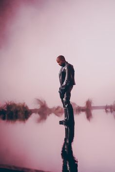 a man standing in front of a body of water with his reflection on the ground