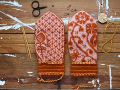 two mitts are sitting on a wooden table next to knitting needles and yarns