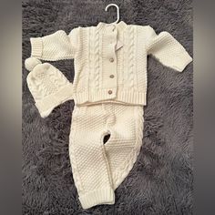 a baby's white knitted outfit and booties laying on a gray carpet