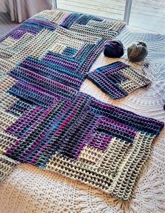 a crocheted blanket on top of a bed next to a ball of yarn