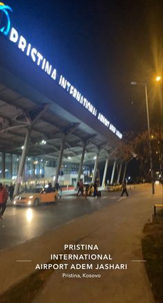 an airport terminal at night with people walking around the building and cars parked in front