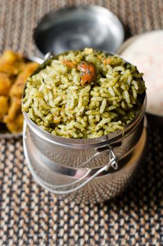 a metal container filled with green rice next to other food on top of a table