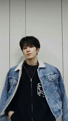 a young man wearing a denim jacket and black t - shirt standing in front of a white wall