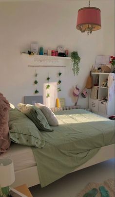 a bed with green sheets and pillows in a bedroom next to a shelf filled with plants