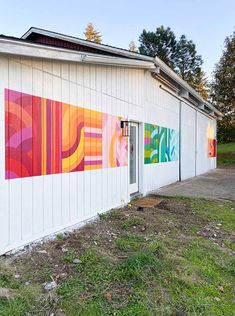 the side of a white building with colorful paintings on it's walls and doors