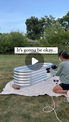 a woman sitting on top of a blanket next to a large metal object in the grass