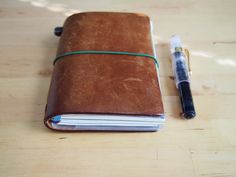 a notebook with a pen on top of it sitting on a wooden table next to an empty notepad