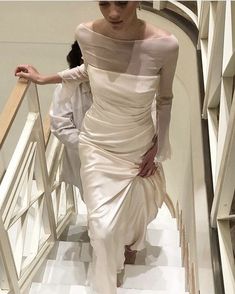 a woman in a white dress is walking down the stairs with her hand on her hip