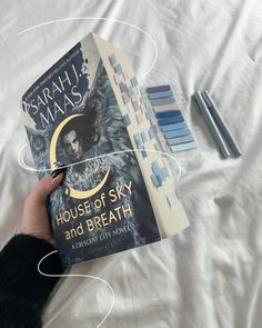 a person holding up a book in front of them on a bed with the title house of sky and breath