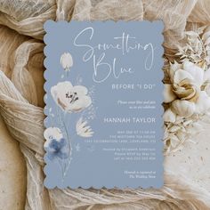 a blue and white wedding card with flowers on the front, sitting next to some fabric