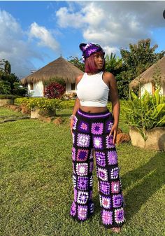 a woman standing in the grass wearing purple and white crocheted pants with flowers on them