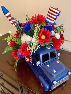 a blue truck with red, white and blue flowers in it's bed sitting on top of a dresser