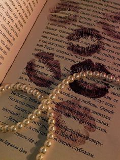 an open book with pearls and lipstick drawn on it's pages, next to a beaded necklace