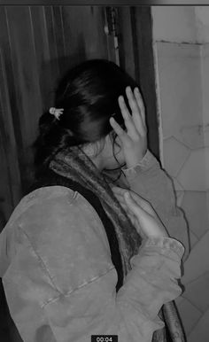 black and white photograph of a woman covering her face with her hands while standing in front of a door