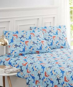 a bed covered in blue and red sheets with shark designs on the sheet set, next to a gold lamp