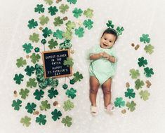 a baby is laying on the floor surrounded by green shamrocks and little chalkboard