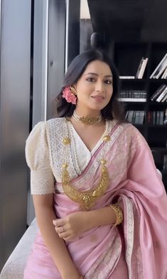 a woman in a pink and white sari sitting on a chair with her arms crossed