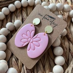 a pair of pink and gold earrings sitting on top of a wooden bead necklace