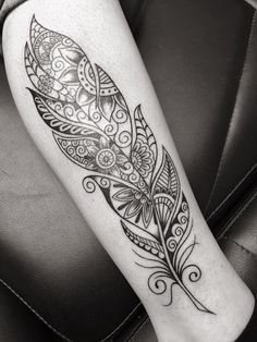 a black and white photo of a tattoo with a feather on the leg, which is decorated