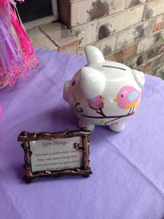 a pink piggy bank sitting on top of a purple table cloth next to a plaque