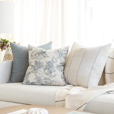 a white couch with blue and white pillows on it's back, in front of a window