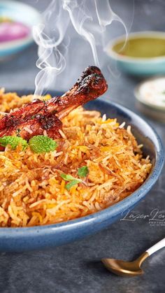 a blue bowl filled with rice and meat on top of a table next to silverware