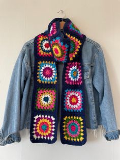 a crocheted jacket hanging on a wall with a denim jacket and jean jacket