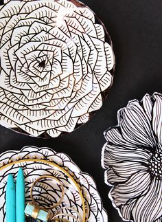 three plates with flowers on them sitting next to pens and markers