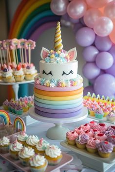 a table topped with lots of cupcakes and cake next to rainbow colored balloons