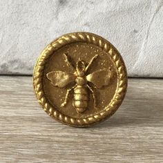 a gold button with a bee on it sitting on top of a wooden table next to a white wall